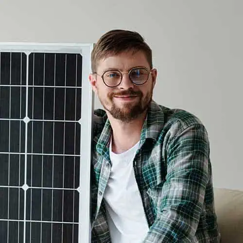 Man holding solar panel, smiling, in a home setting.